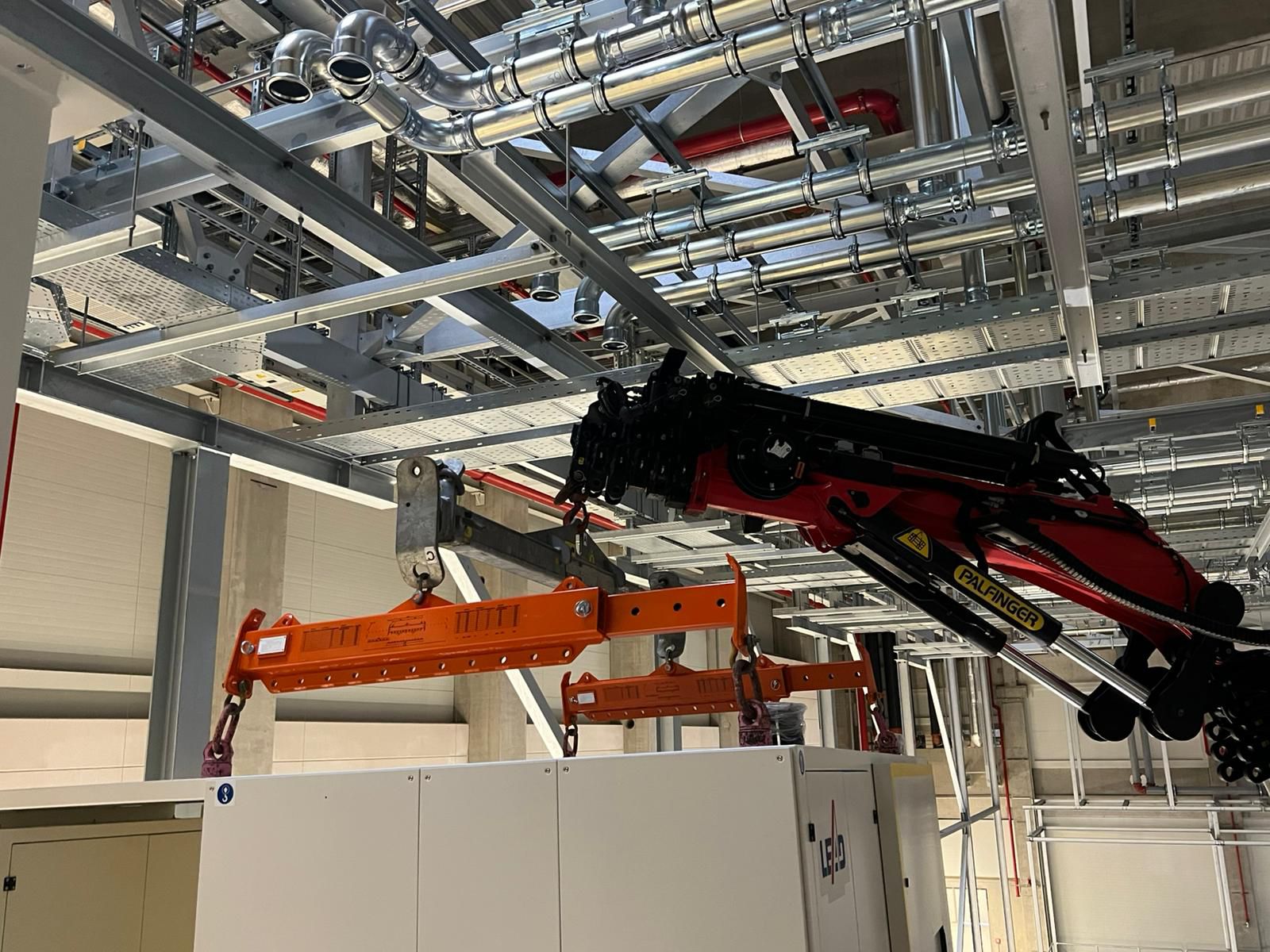 Montagearbeiten im Deckenbereich mit hydraulischem Minikran zwischen Leitungen.
