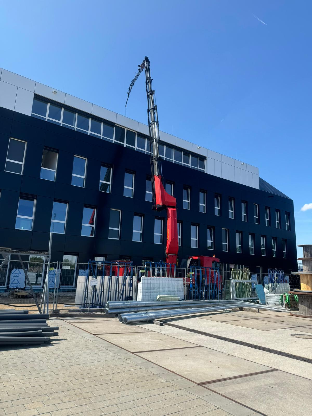 Mobilkran hebt Bauteile auf ein modernes Firmengebäude.